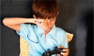 the little boy rubbing his one eye while playing video games. 